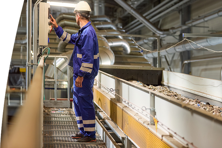 A technician wearing blue overalls and a white helmet operates machinery at an industrial recycling facility where he manages the sorting and processing of refuse-derived fuel (RDF) on a conveyor belt